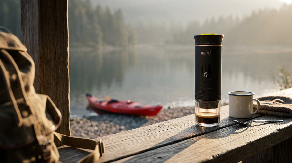 Black Brulé espresso maker with fresh espresso on a weathered lakeside rail, a kayak on the shore behind