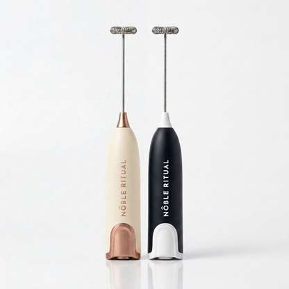 Noble Frothé Set of 2 in Cream & Black: a cream frother with rose-gold collar and base and a black frother with white collar and base, each with a vertical NÔBLE RITUAL wordmark and a coiled steel whisk