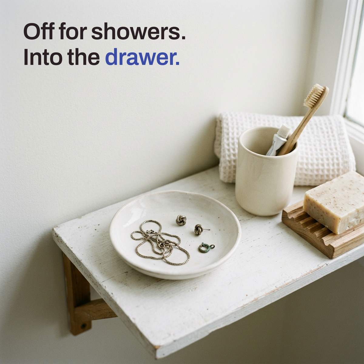 A small dish on a bathroom shelf holding tangled, dull chains and two small earrings