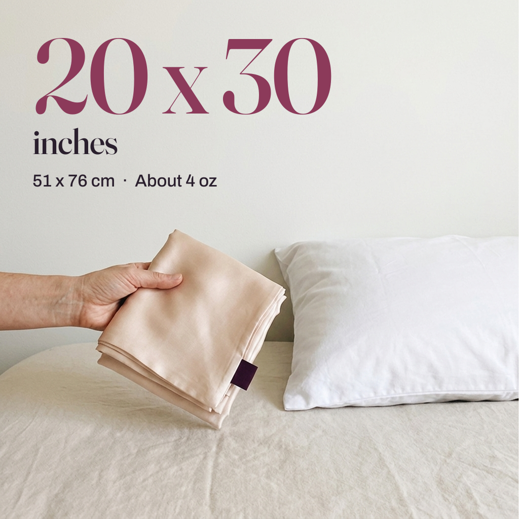 20 x 30 inches. A hand holds a folded champagne silk pillowcase beside a standard pillow, 51 x 76 cm, about 4 oz