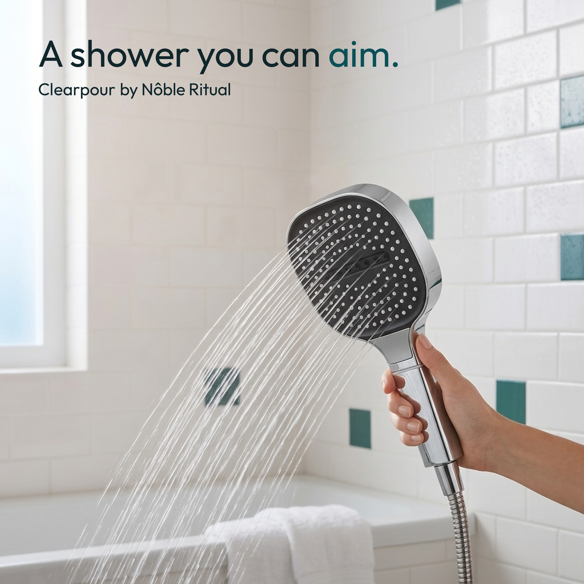 A hand holding the Clearpour showerhead in a tiled shower, water falling toward the tub
